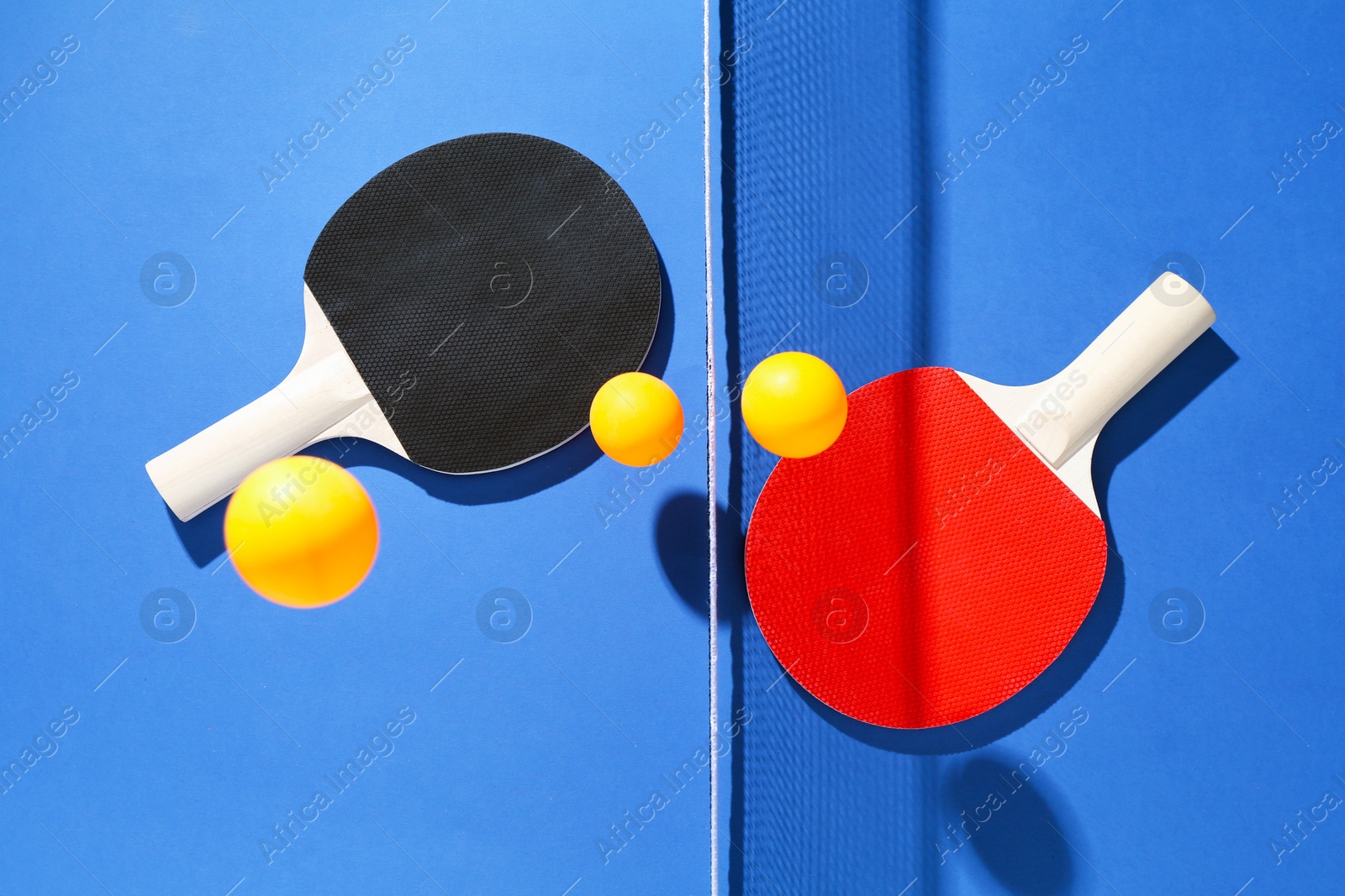 Ping pong rackets, balls and net on blue background, flat lay Photo of Ping pong rackets, balls and net on blue background, flat lay