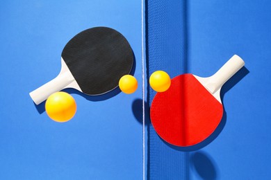 Photo of Ping pong rackets, balls and net on blue background, flat lay