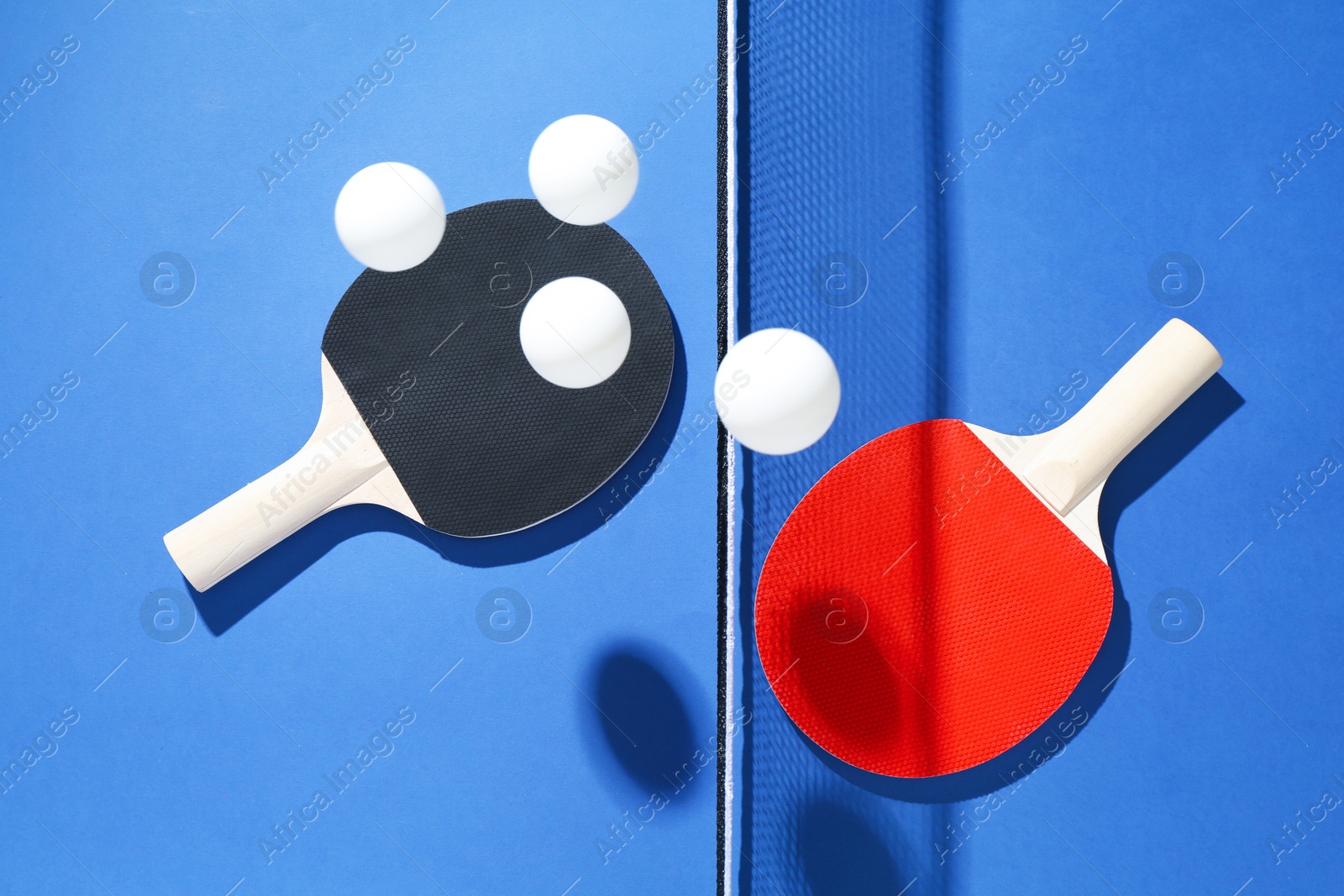 Ping pong rackets, balls and net on blue background, flat lay Photo of Ping pong rackets, balls and net on blue background, flat lay