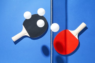 Photo of Ping pong rackets, balls and net on blue background, flat lay