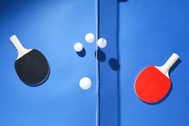 Photo of Ping pong rackets, balls and net on blue background, flat lay