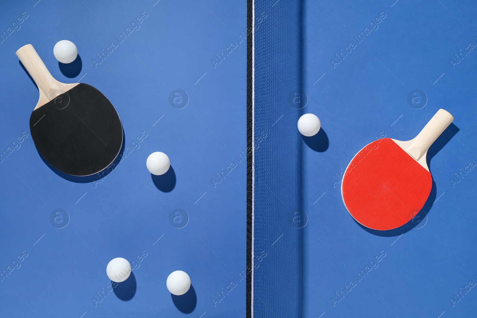 Ping pong rackets, balls and net on blue background, flat lay Photo of Ping pong rackets, balls and net on blue background, flat lay