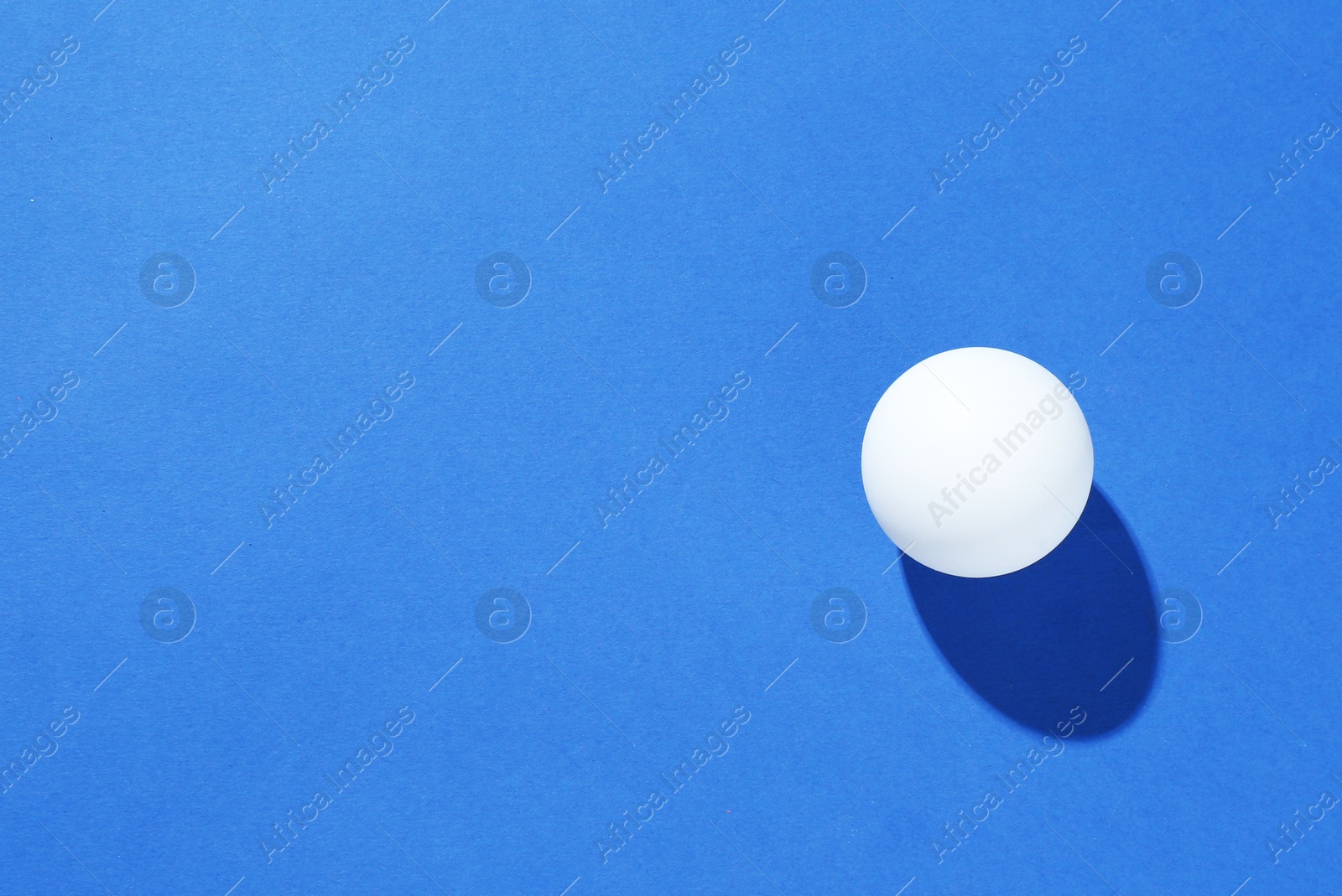 One ping pong ball on blue background, top view. Space for text Photo of One ping pong ball on blue background, top view. Space for text