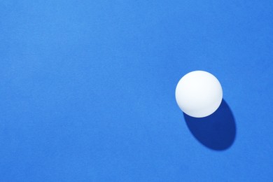 Photo of One ping pong ball on blue background, top view. Space for text