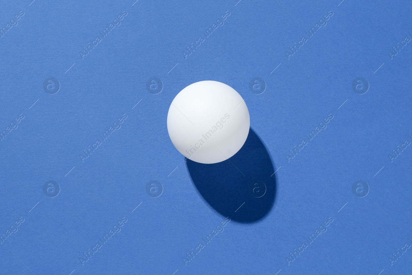 One ping pong ball on blue background, top view Photo of One ping pong ball on blue background, top view