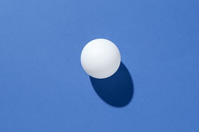 Photo of One ping pong ball on blue background, top view