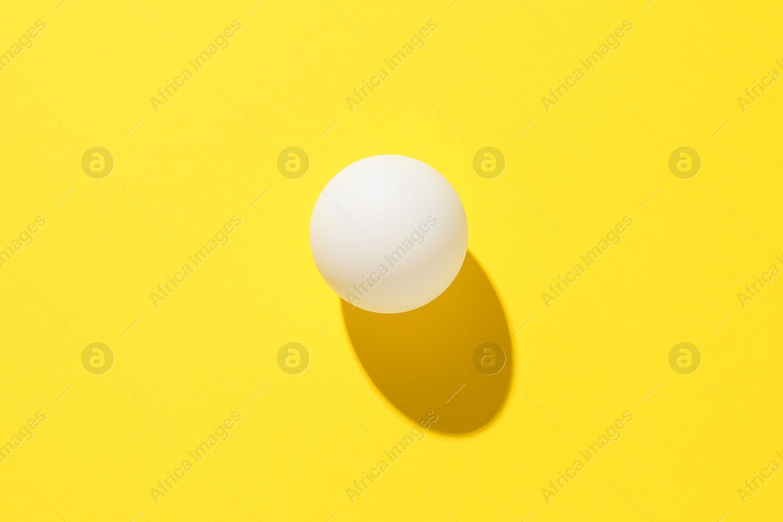 One ping pong ball on yellow background, top view Photo of One ping pong ball on yellow background, top view