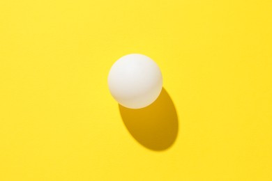Photo of One ping pong ball on yellow background, top view
