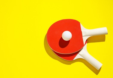 Photo of Ping pong rackets and ball on yellow background, top view. Space for text