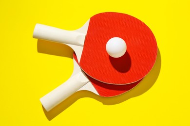Photo of Ping pong rackets and ball on yellow background, top view