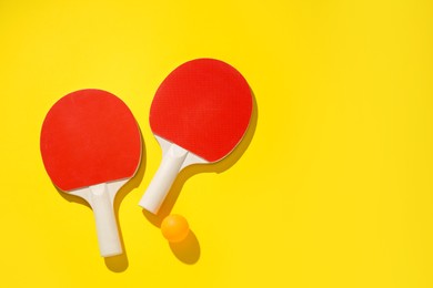 Photo of Ping pong rackets and ball on yellow background, top view. Space for text