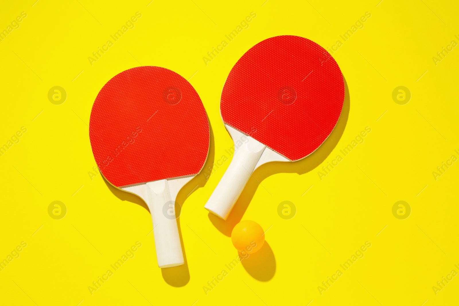 Ping pong rackets and ball on yellow background, top view Photo of Ping pong rackets and ball on yellow background, top view