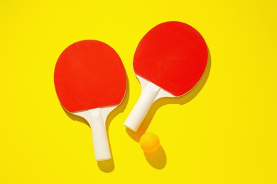 Photo of Ping pong rackets and ball on yellow background, top view