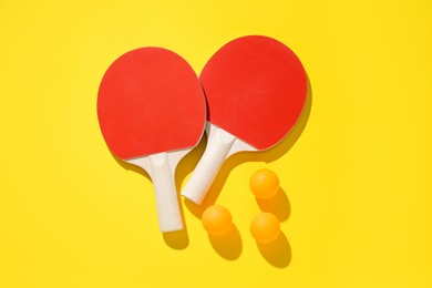 Photo of Ping pong rackets and balls on yellow background, flat lay