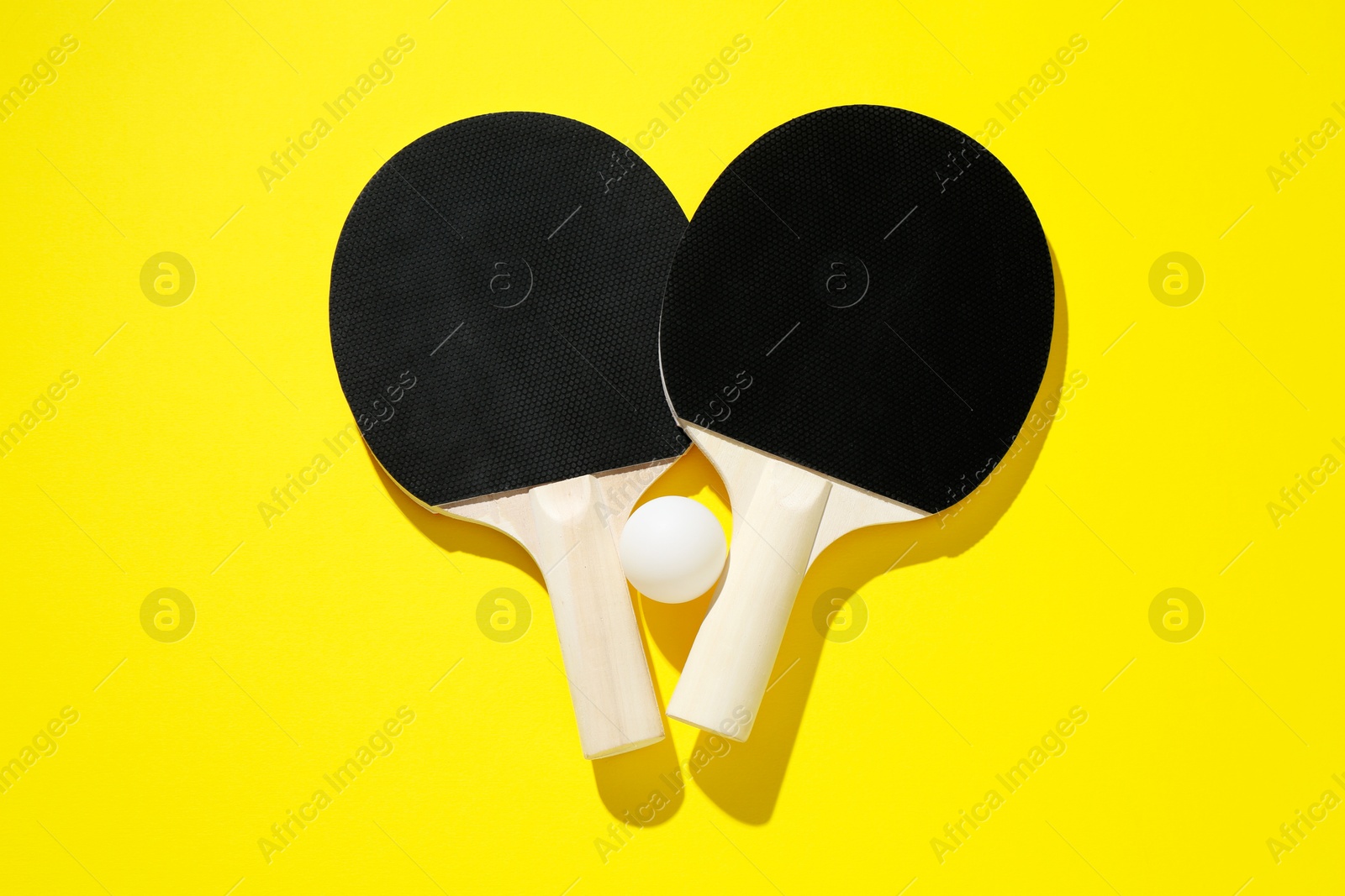 Ping pong rackets and ball on yellow background, top view Photo of Ping pong rackets and ball on yellow background, top view