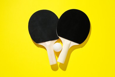 Photo of Ping pong rackets and ball on yellow background, top view