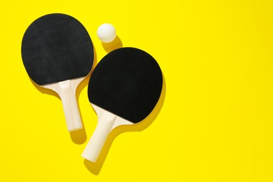 Photo of Ping pong rackets and ball on yellow background, top view. Space for text