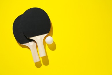 Photo of Ping pong rackets and ball on yellow background, top view. Space for text