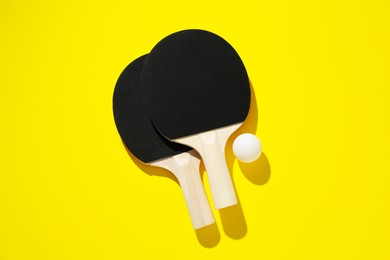 Photo of Ping pong rackets and ball on yellow background, top view