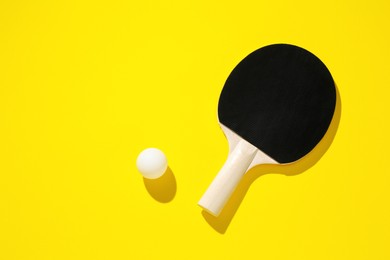 Photo of Ping pong racket and ball on yellow background, top view. Space for text