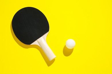 Photo of Ping pong racket and ball on yellow background, top view. Space for text