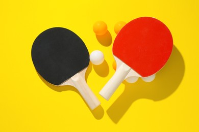 Photo of Ping pong rackets and balls on yellow background, flat lay