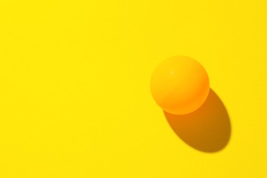 Photo of One ping pong ball on yellow background, top view. Space for text