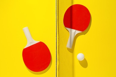 Photo of Ping pong rackets, ball and net on yellow background, flat lay