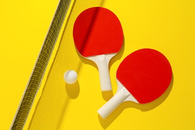 Photo of Ping pong rackets, ball and net on yellow background, flat lay