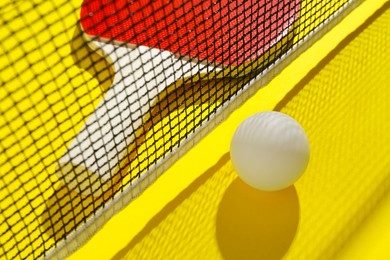 Photo of Ping pong racket, ball and net on yellow background, closeup