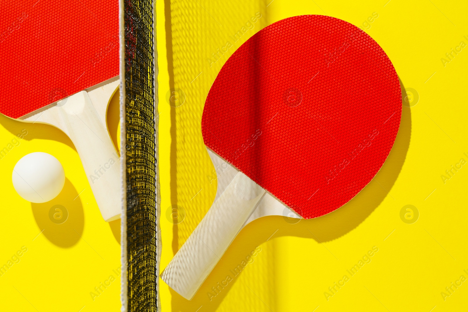 Ping pong rackets, ball and net on yellow background, flat lay Photo of Ping pong rackets, ball and net on yellow background, flat lay