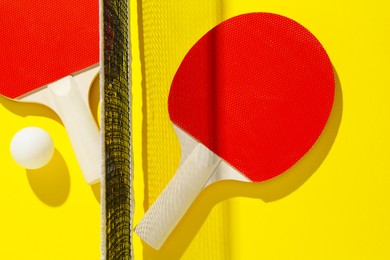 Photo of Ping pong rackets, ball and net on yellow background, flat lay