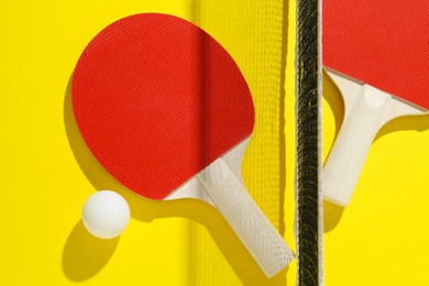 Photo of Ping pong rackets, ball and net on yellow background, flat lay