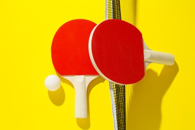 Photo of Ping pong rackets, ball and net on yellow background, flat lay
