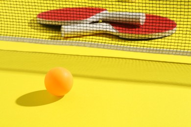 Photo of Ping pong rackets, ball and net on yellow background