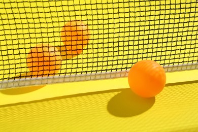 Photo of Ping pong balls and net on yellow background, closeup