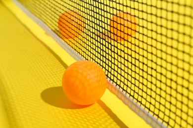 Photo of Ping pong balls and net on yellow background, closeup