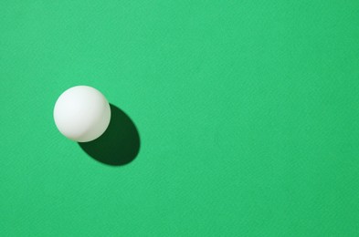 Photo of One ping pong ball on green background, top view. Space for text