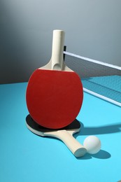 Photo of Ping pong rackets, ball and net on light blue table