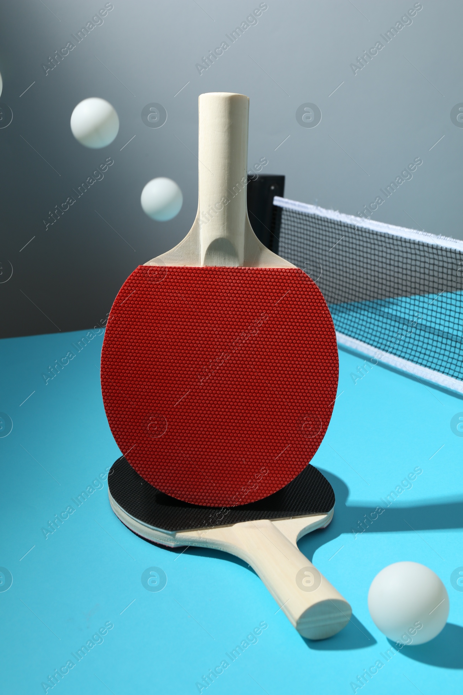 Ping pong rackets, balls and net on light blue table Photo of Ping pong rackets, balls and net on light blue table