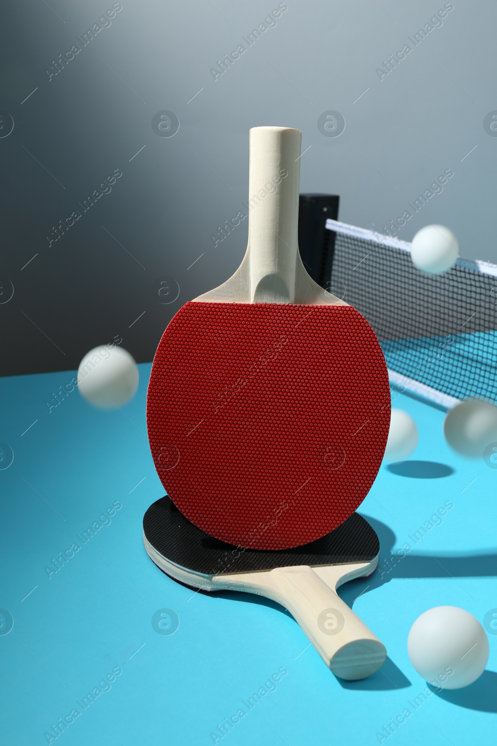Ping pong rackets, balls and net on light blue table Photo of Ping pong rackets, balls and net on light blue table