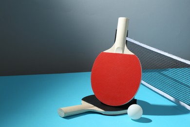 Photo of Ping pong rackets, ball and net on light blue table. Space for text