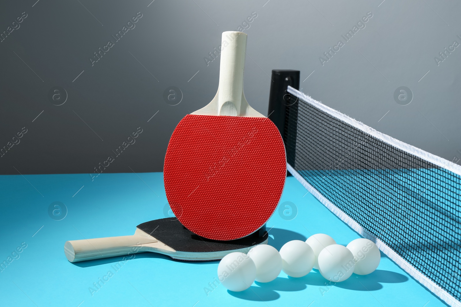 Ping pong rackets, balls and net on light blue table Photo of Ping pong rackets, balls and net on light blue table