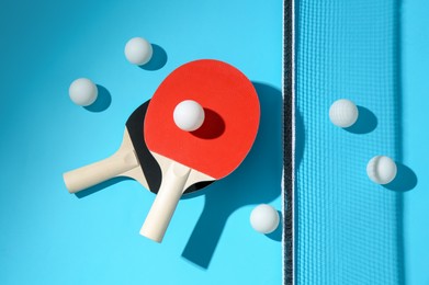 Photo of Ping pong rackets, balls and net on light blue background, flat lay