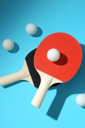 Photo of Ping pong rackets and balls on light blue background, flat lay
