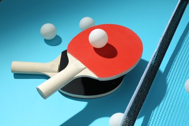 Photo of Ping pong rackets, balls and net on light blue background, closeup