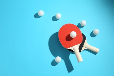 Photo of Ping pong rackets and balls on light blue background, flat lay. Space for text