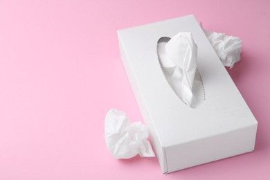 Photo of Box with paper handkerchiefs and crumpled tissues on pink background, closeup. Space for text