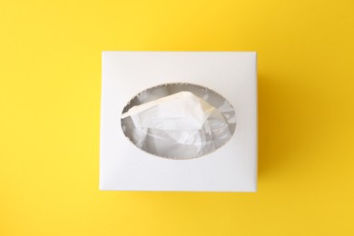Photo of Box with paper handkerchiefs on yellow background, top view