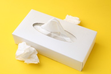 Photo of Box with paper handkerchiefs and crumpled tissues on yellow background, closeup